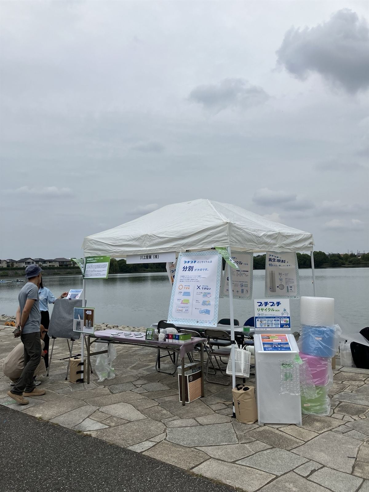 湖のそばに立つ川上産業のブース。プチプチのリサイクルを紹介するパネルとリサイクルBOXが並ぶ